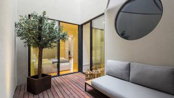 A modern interior with a wooden floor, a grey sofa, a potted tree, and a large window.