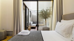 Habitación de hotel con cama, una pequeña zona de estar con sofá y mesa, una planta en maceta y vistas a través de un ventanal.