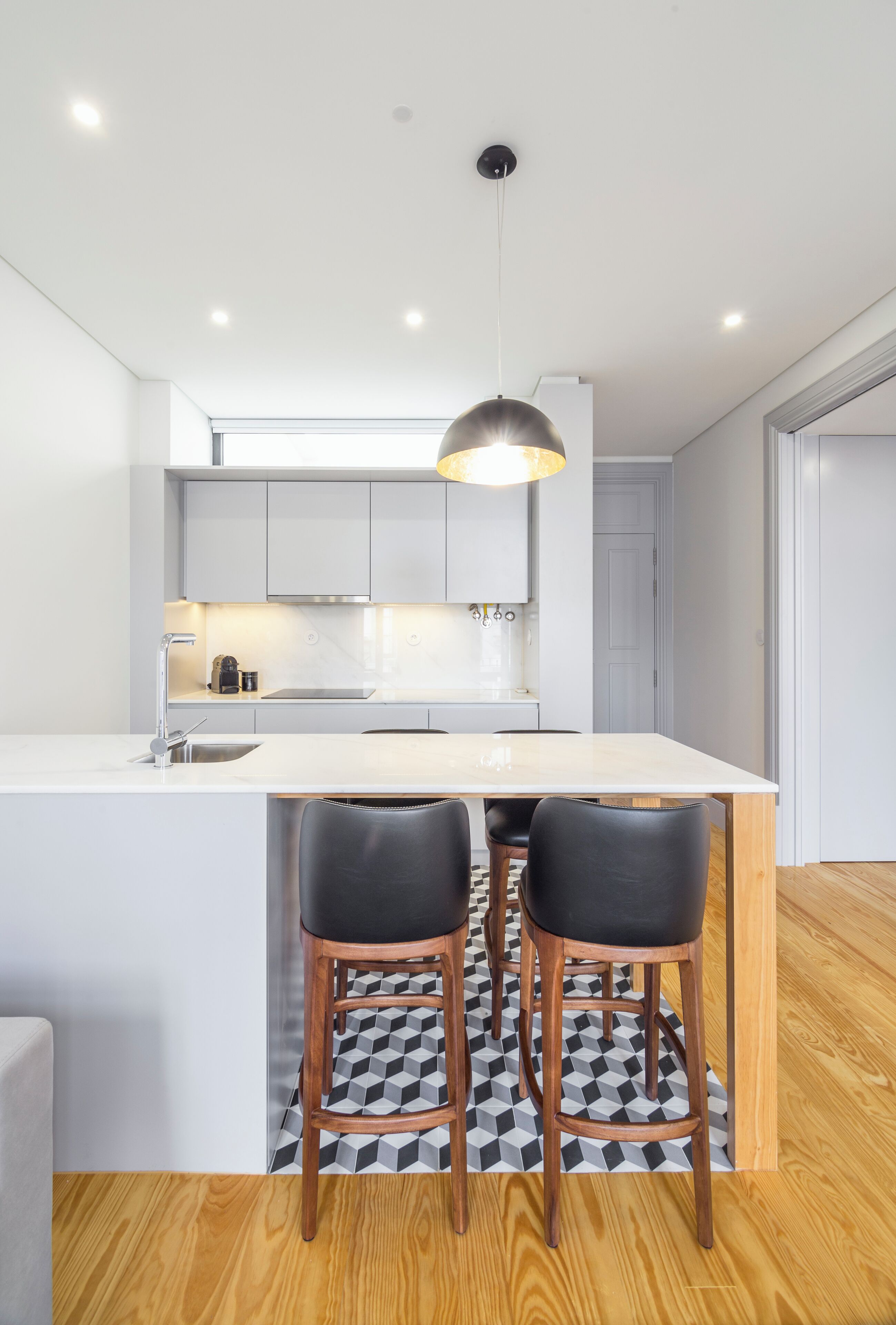 A modern kitchen with a central island, two bar stools, and a pendant light.