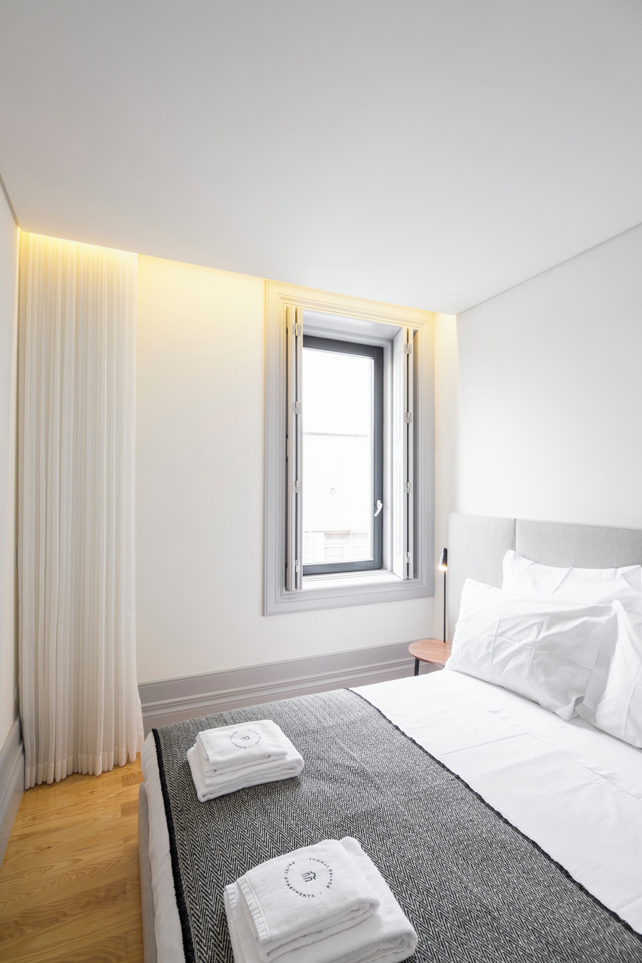 Een moderne hotelkamer met een opgemaakt bed, een raam met gordijnen en een nachtkastje met een lamp.