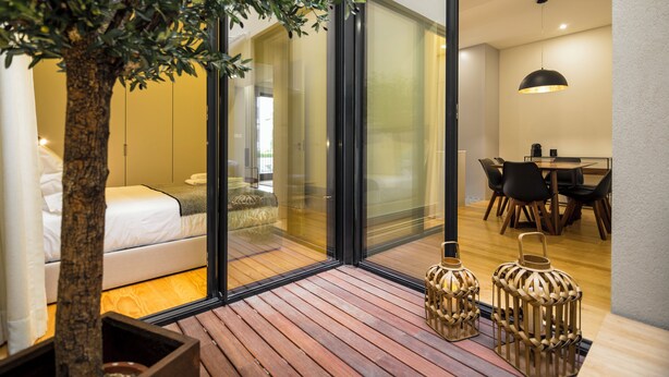 Un interior moderno con cubierta de madera, cama, zona de comedor y ventana grande.