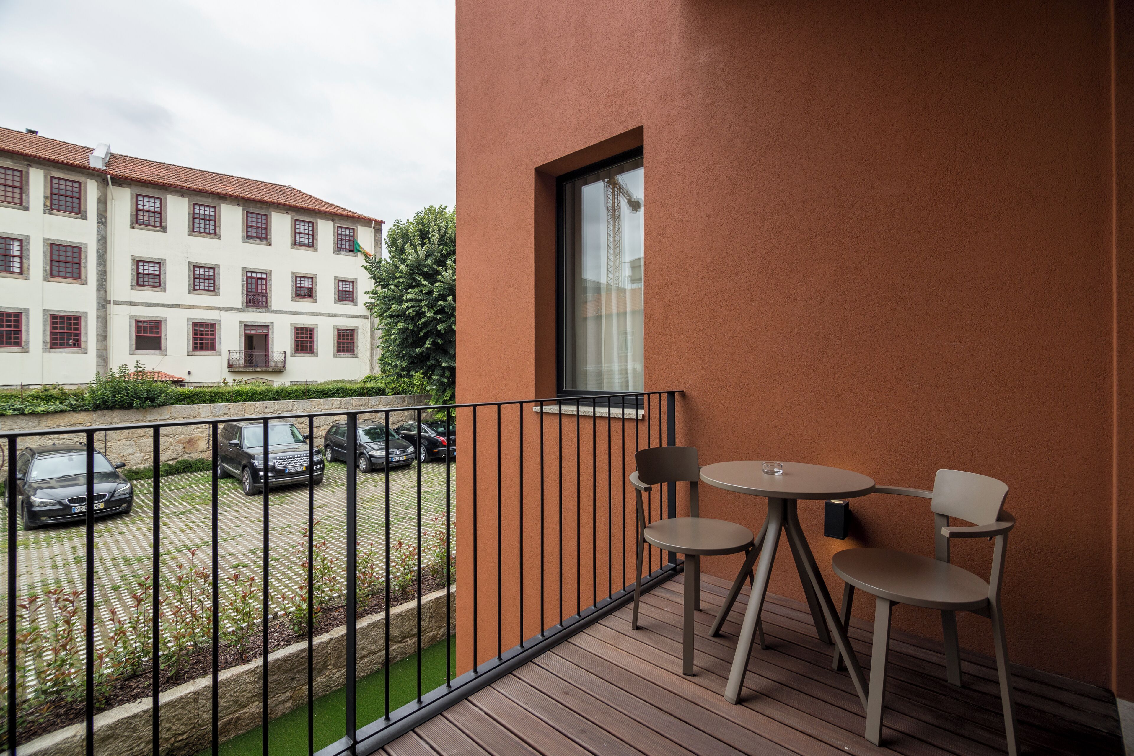 Ein Balkon mit Tisch und Stühlen, Blick auf geparkte Autos und ein Gebäude im Hintergrund.