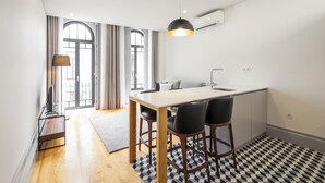 Una cocina moderna con comedor, que incluye una lámpara colgante negra, un taburete pequeño y vistas al exterior a través de amplias ventanas.