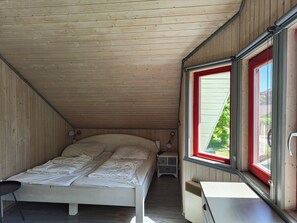 Una cama individual con cabecera, una mesita de noche y una ventana con marco rojo.