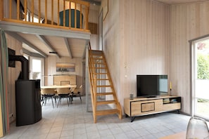 Una habitación amplia con una escalera de madera, un comedor y un televisor sobre un mueble de madera.