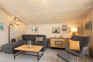 Una habitación acogedora con sofá, sillón y una mesita. Hay un mueble con espejo y una lámpara.