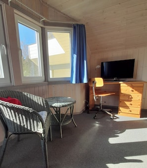 Une pièce équipée d’une télévision, d’un bureau, d’une chaise et d’une fenêtre avec des rideaux.