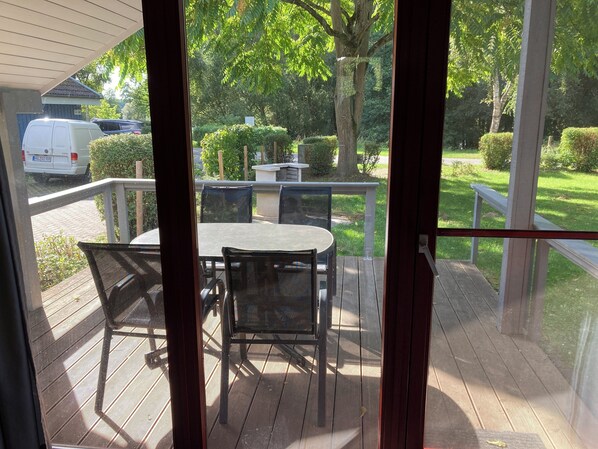 Ein überdachter Außenbereich mit Tisch und Stühlen, ein weißer Van im Hintergrund und Blick auf eine grüne Landschaft mit Bäumen und einem Weg.