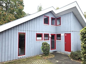 Un edificio de dos pisos con fachada gris y ventanas de marco rojo.