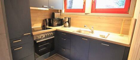 A compact kitchen with dark cabinets, a sink, a stove, and a microwave.