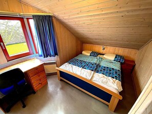 Una habitación pequeña con paneles de madera, una cama, un escritorio y una ventana con cortinas.