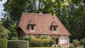 A traditional half-timbered house with a steeply pitched roof, two small windows, and a front porch with a bench. - Locations - Domaine Le Coq Enchanté (Cambremer)