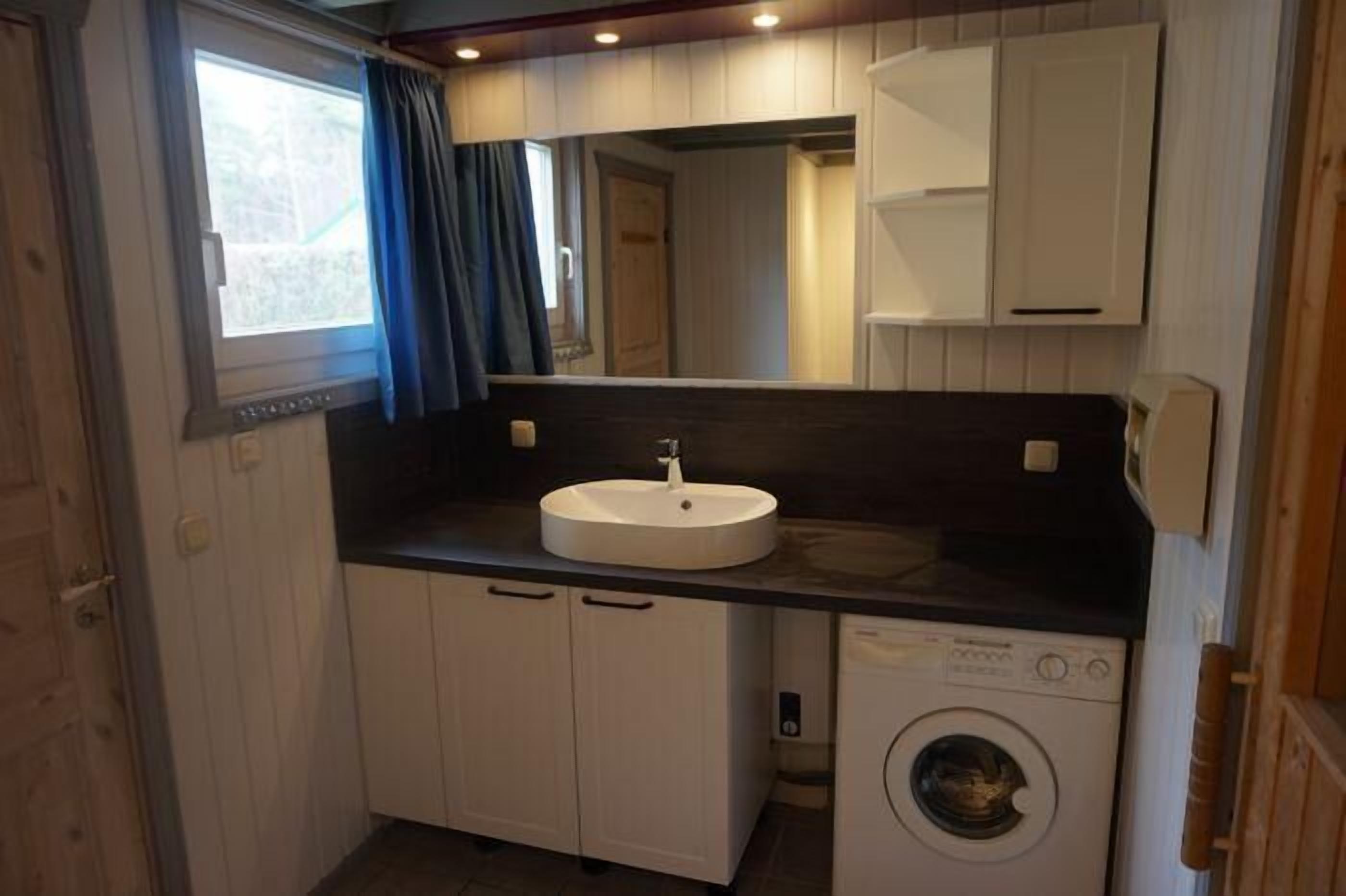 Ein kleines Badezimmer mit Waschbecken, Spiegel, Schränken und einer Waschmaschine.