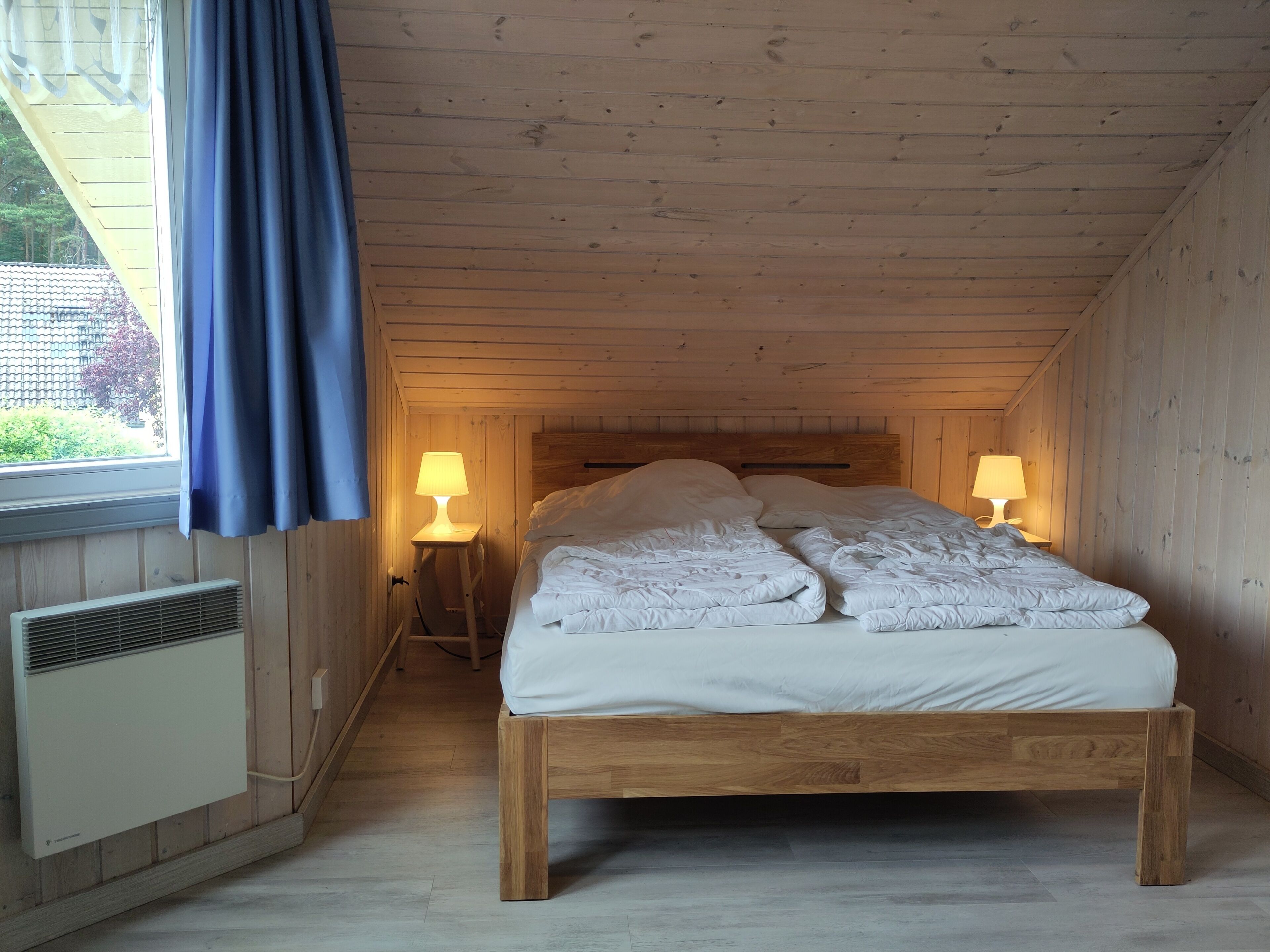 A wooden-paneled bedroom with a bed, two bedside lamps, and a window with curtains.