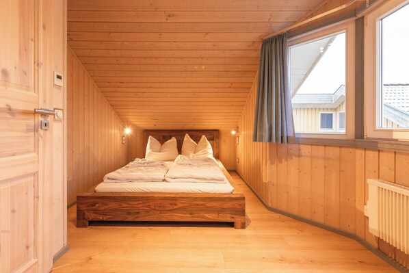 A wooden-paneled room with a bed, a window with curtains, and a radiator.