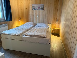 A double bed with white bedding, wooden panel walls, a small bedside table with a lamp, and a decorative sign above the bed. - Wildgans 218 - Klassisches Skandinavisches Ferienhaus für bis zu 6 Personen (Mirow)