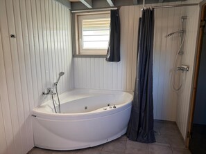 Een badkamer met een vrijstaand bad, een douche en een raam met zonwering.