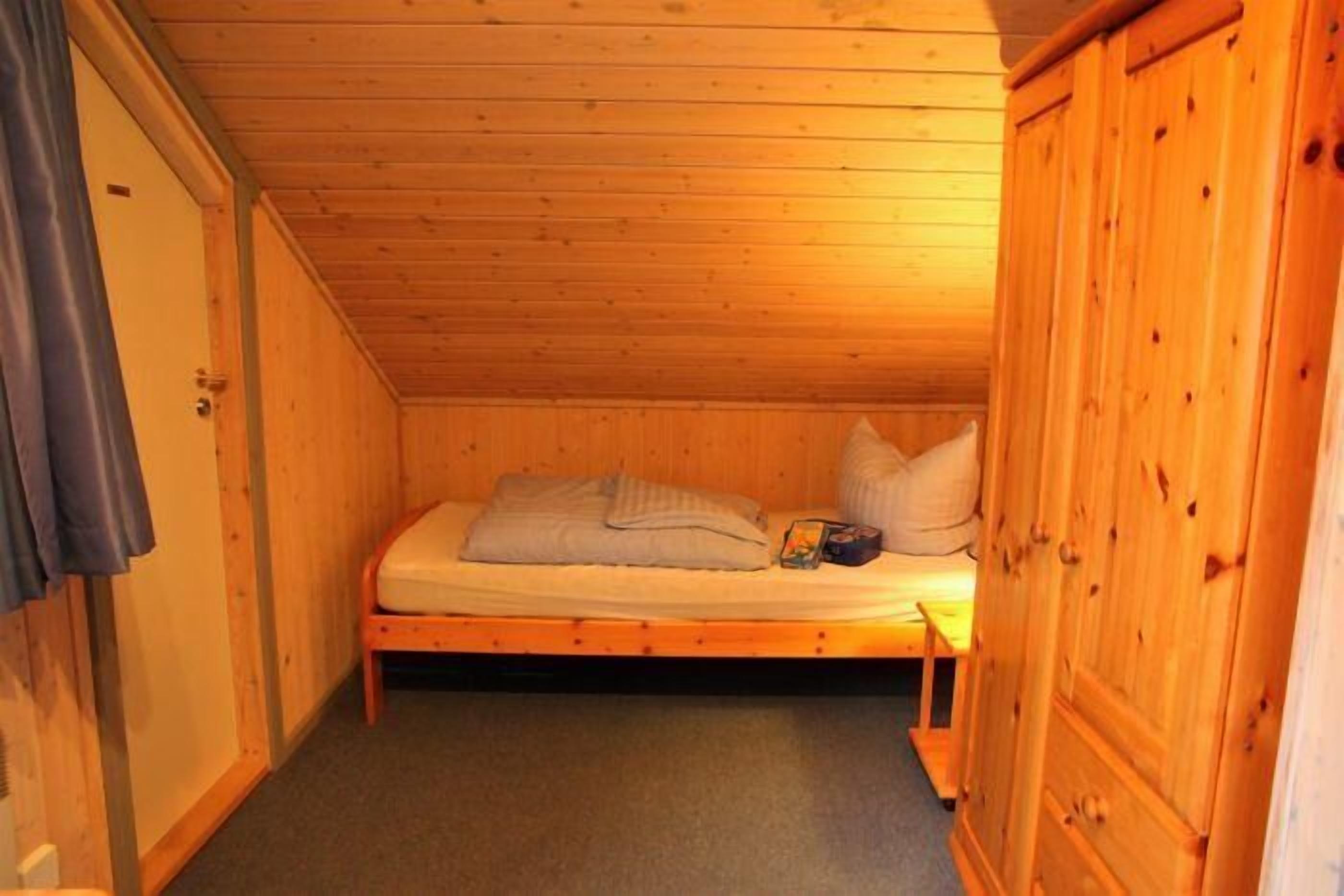A small, single-bed room with wooden walls and a sloped ceiling.