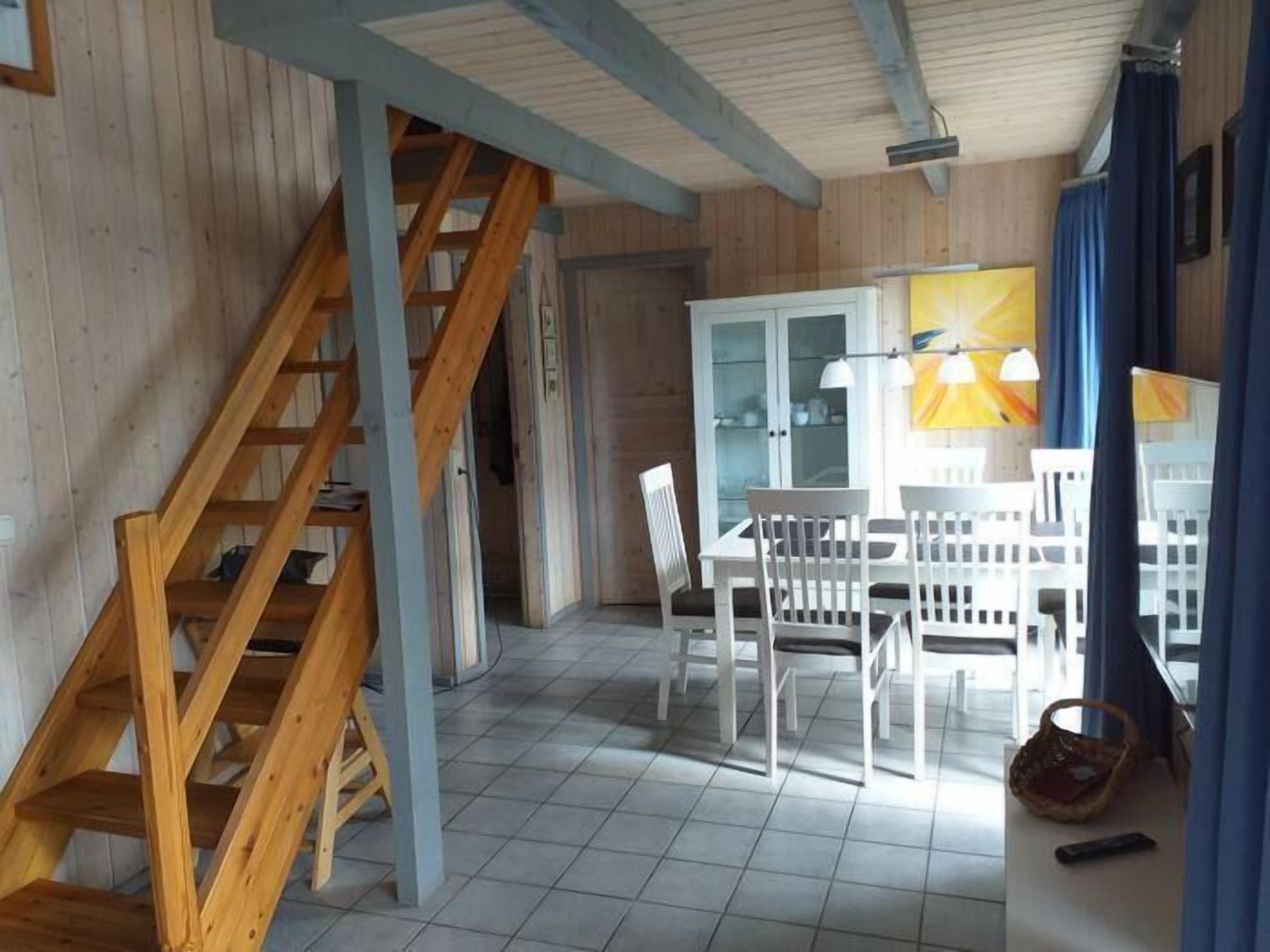 Interior em madeira com escada, área de jantar com mobiliário branco e um armário com portas de vidro.