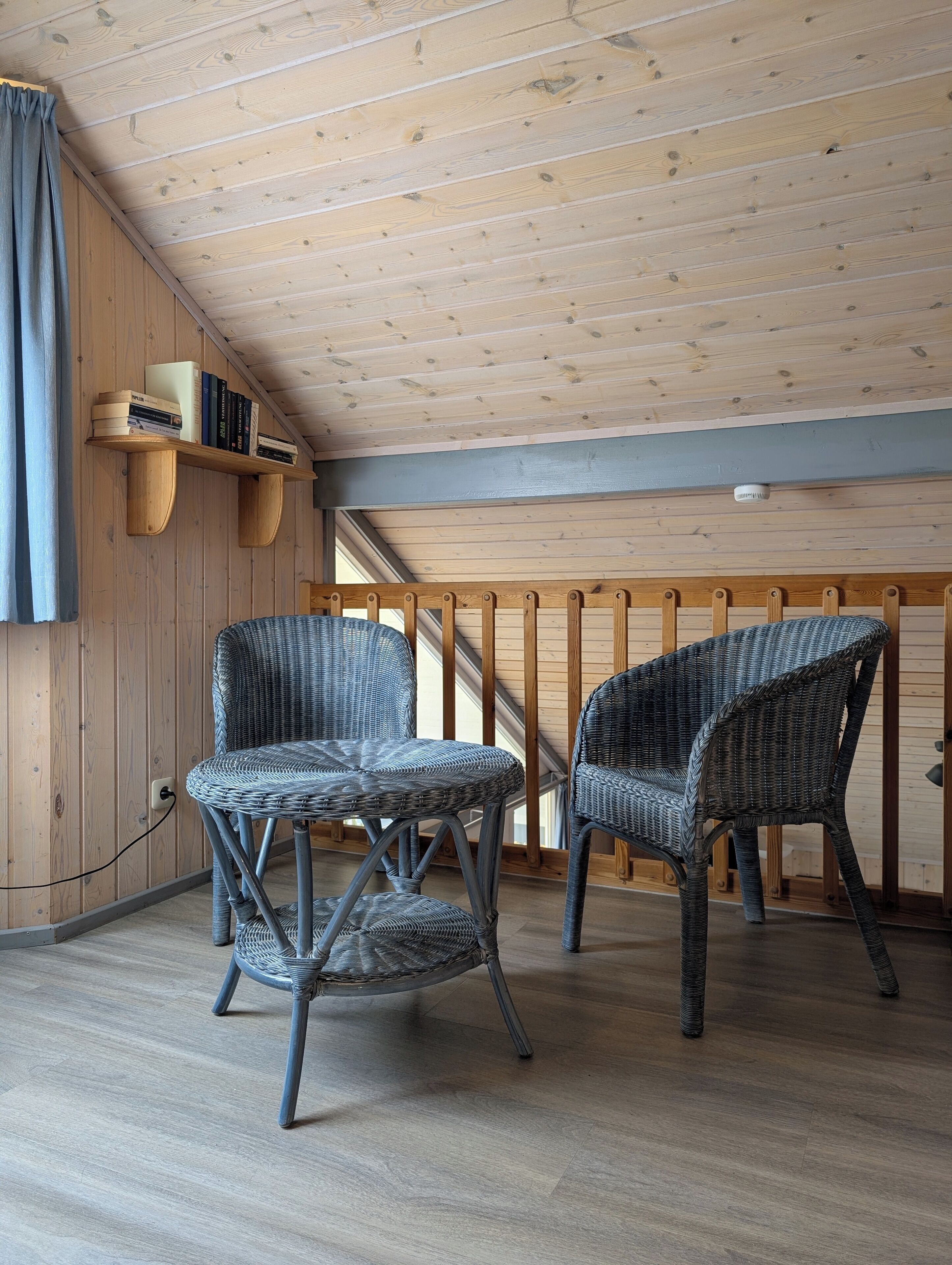 A room with wooden walls and ceiling, two wicker chairs, a bookshelf, and a power outlet.