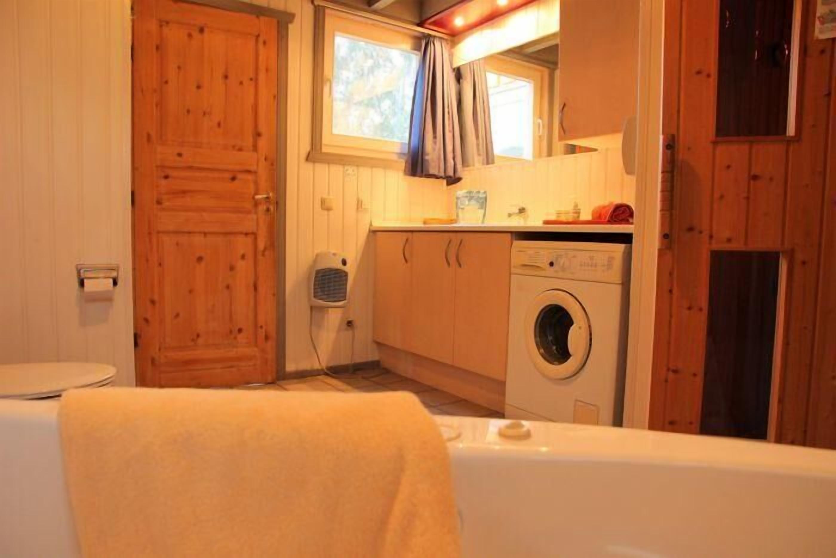 Habitación pequeña con puerta de madera, lavadora, ventana con cortinas y una toalla en el suelo.