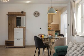 A modern kitchen with wooden cabinets, a dining table with chairs, and a hanging light fixture. - Betty Sea View Apartment With Balcony (Vrbnik)