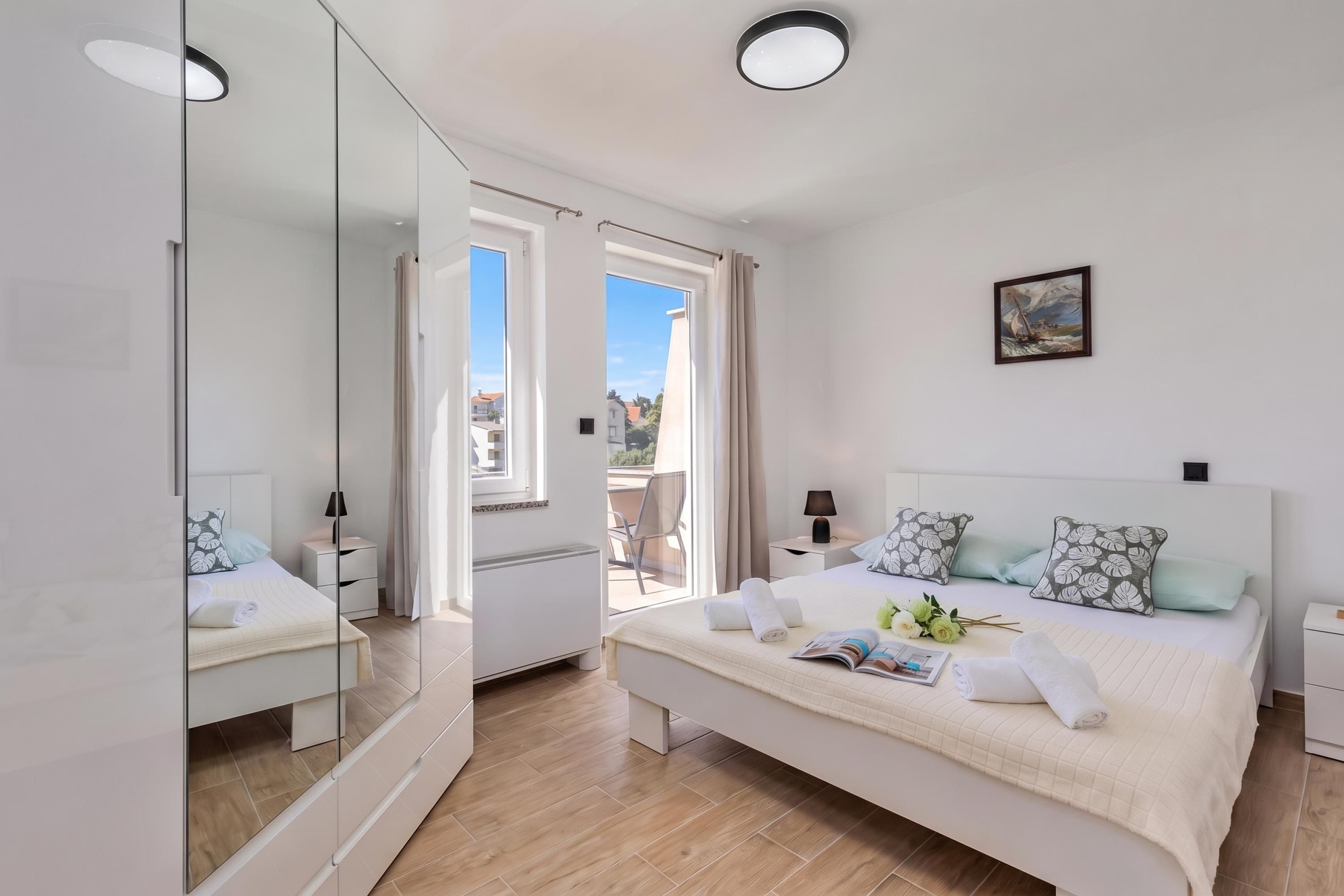 A modern bedroom with a large bed, bedside tables, a mirror, and a view of the outdoors.
