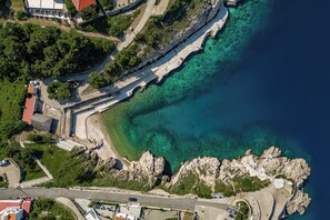An aerial view of a coastal area with a paved walkway along the water, rocky terrain, and buildings with red roofs. - Betty Sea View Apartment With Balcony (Vrbnik)