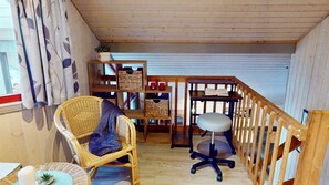 A room with a wicker chair, a small table, a desk with a chair, a bookshelf, and a staircase. - Wildgans 2 - Klassisches Skandinavisches Ferienhaus für bis zu 6 Personen (Mirow)