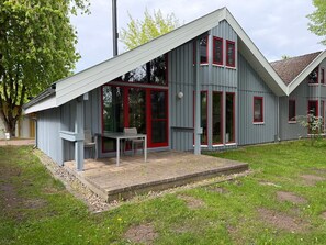Ein modernes Haus mit Satteldach, großen Fenstern und einer kleinen Terrasse mit Tisch und Stühlen.