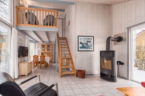Un intérieur chaleureux avec une chambre en mezzanine, un coin repas et un poêle à bois.
