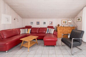Un salon avec un canapé en cuir rouge, une table basse en bois et un fauteuil noir. On y trouve également un meuble en bois orné d’objets décoratifs et des tableaux encadrés accrochés au mur.