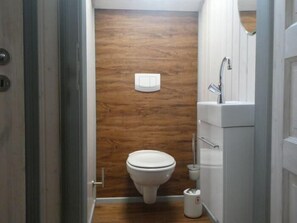 Une petite salle de bain avec un mur en bois, des toilettes, un lavabo et une poubelle.
