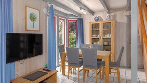 Un coin repas avec une table et des chaises en bois, un téléviseur fixé au mur et un meuble avec des portes en verre.