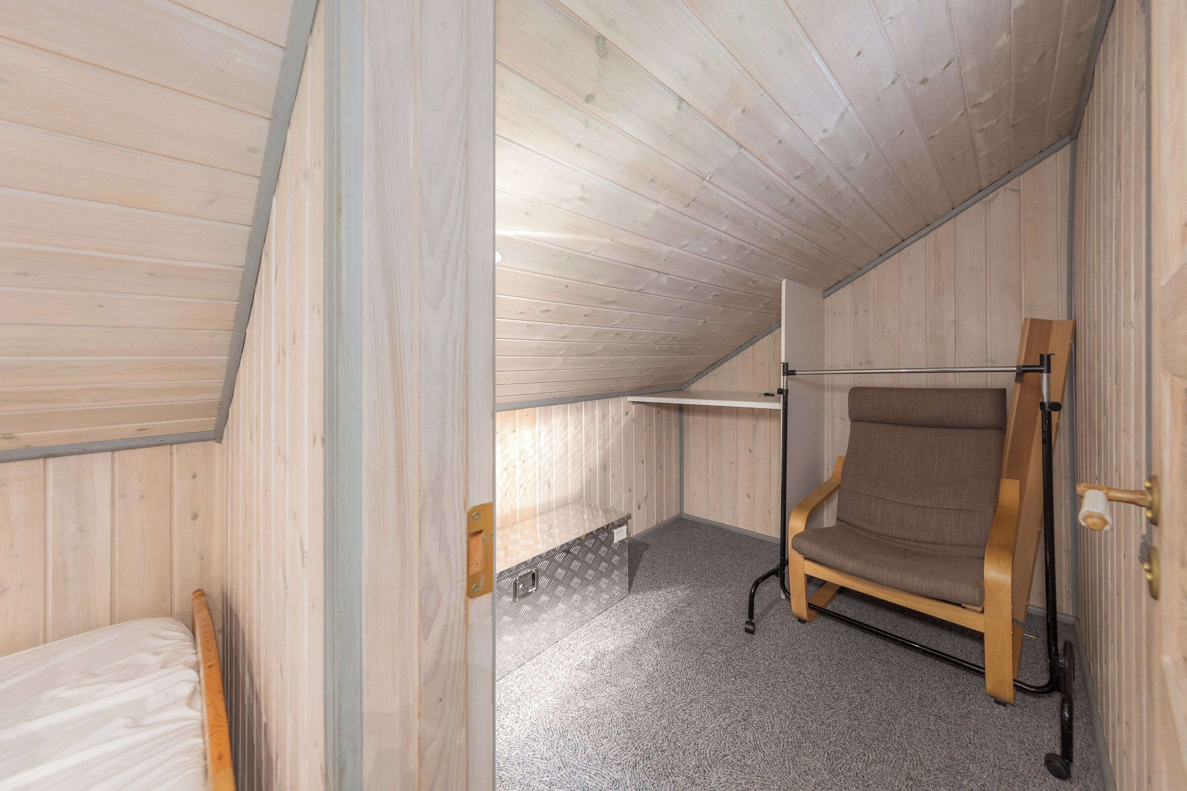 Un pequeño cuarto ático con paneles de madera, una cama litera, una silla y una mesita.
