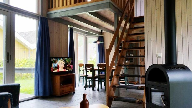 A cozy living room with a television, wooden furniture, a fireplace, and a staircase leading to an upper level.