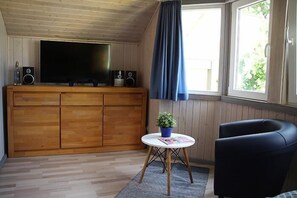 Enjoy a warm and inviting space with a large flat-screen TV, dining table, and comfortable chair.