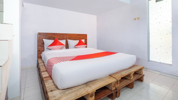 Cama com cabeceira de madeira, roupa de cama branca e detalhes vermelhos.