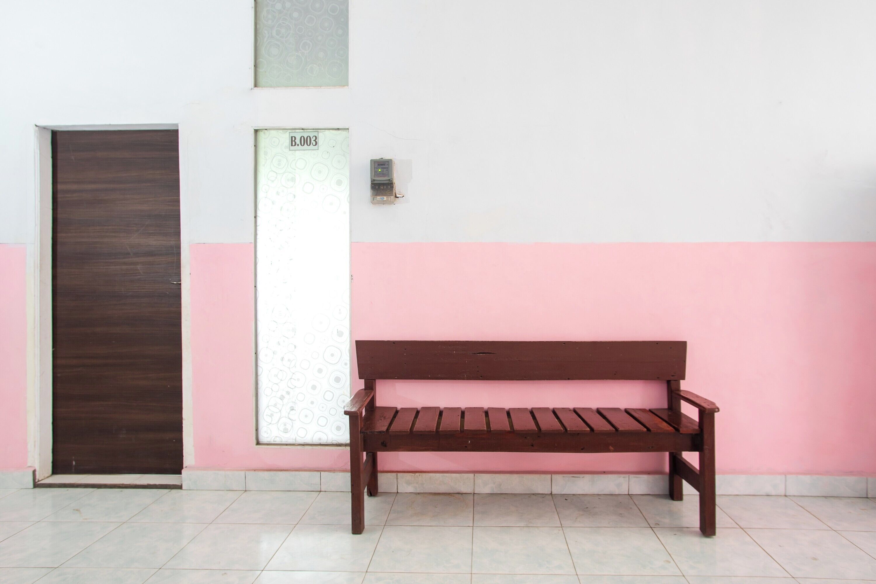 A wooden bench against a wall with a door and a wall-mounted device.