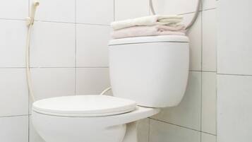 A white toilet with a shower head mounted on the wall above it.