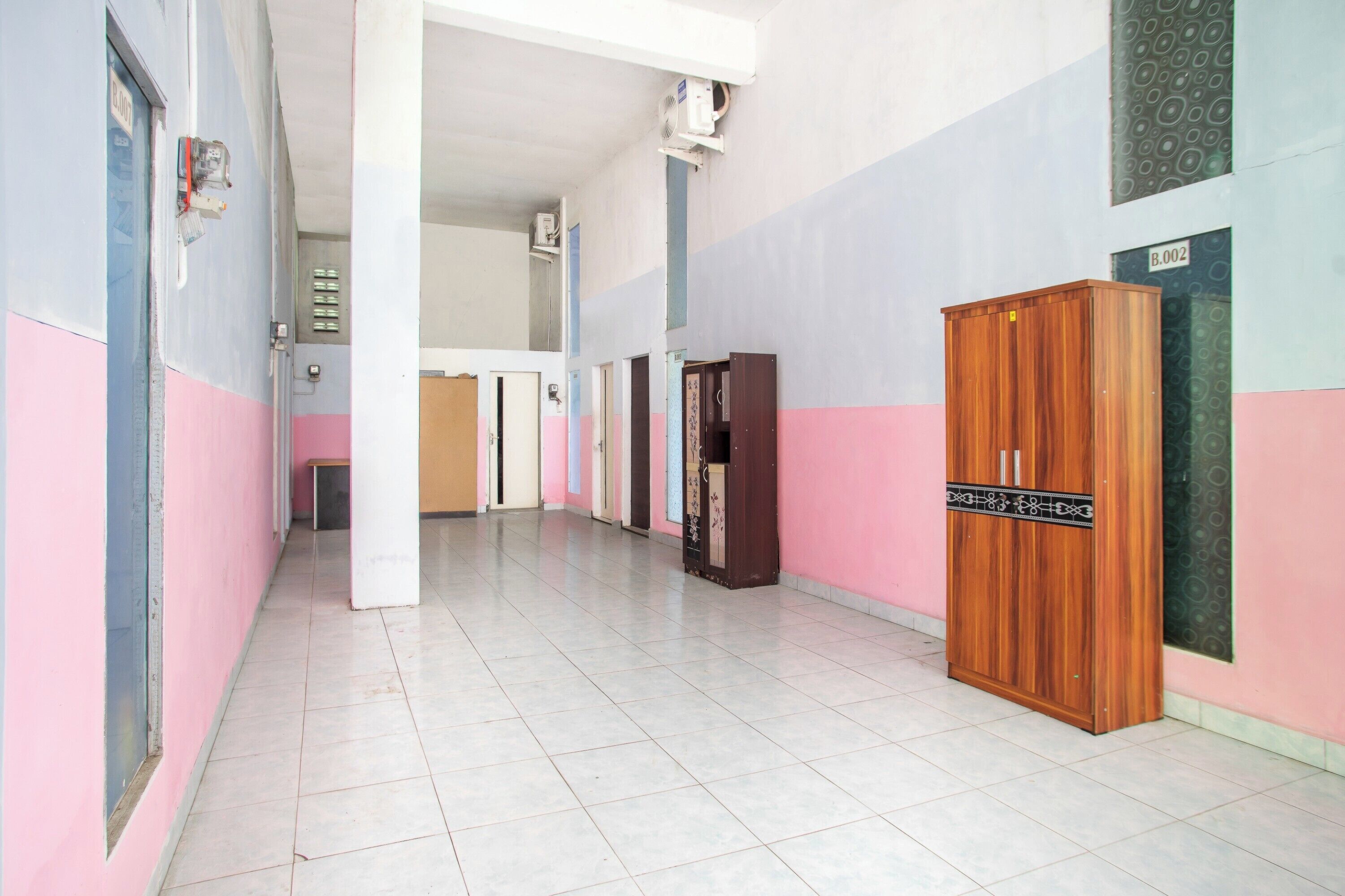 Un couloir aux murs roses et bleus, avec une armoire en bois et un sol carrelé.