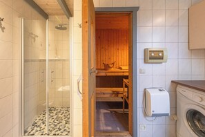 Relax in a compact bathroom with a shower enclosure and adjacent sauna, featuring a washing machine for self-service laundry.