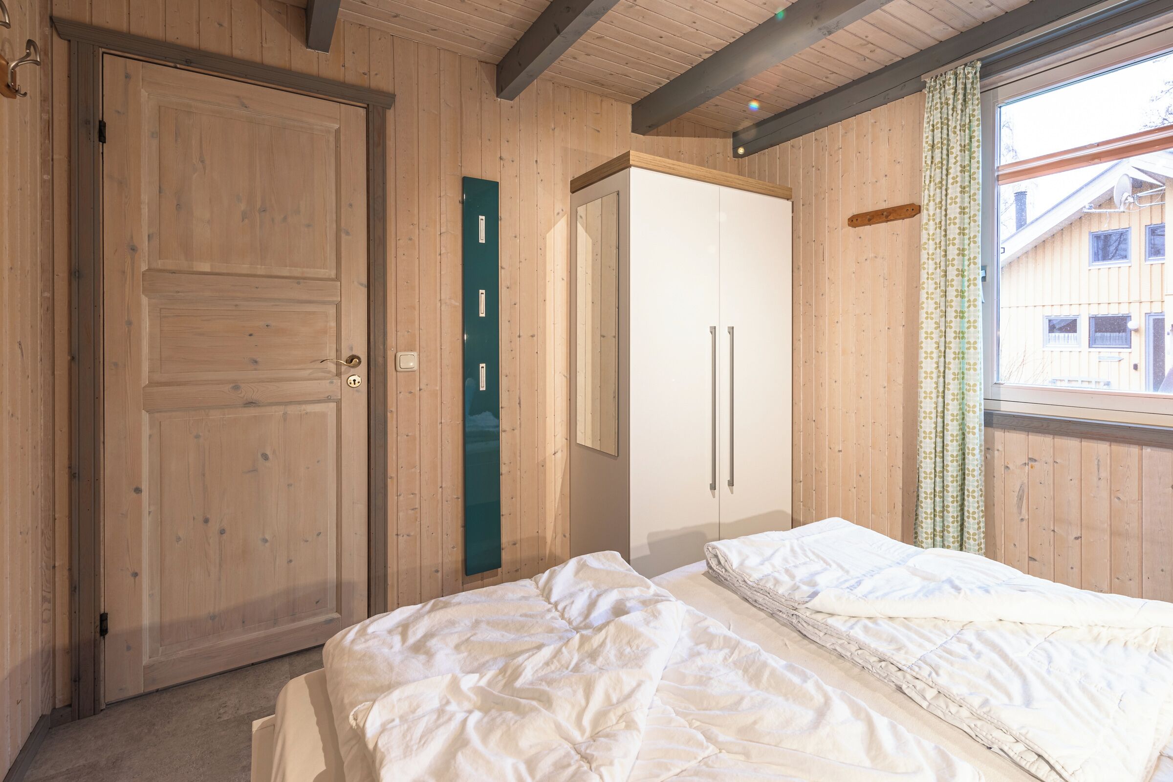 Een slaapkamer met houten wanden, een bed, een kledingkast en een raam met gordijnen.