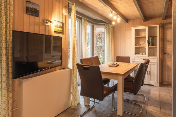A cozy dining area with a wooden table, brown chairs, a flat-screen TV, and a cabinet with glass doors.