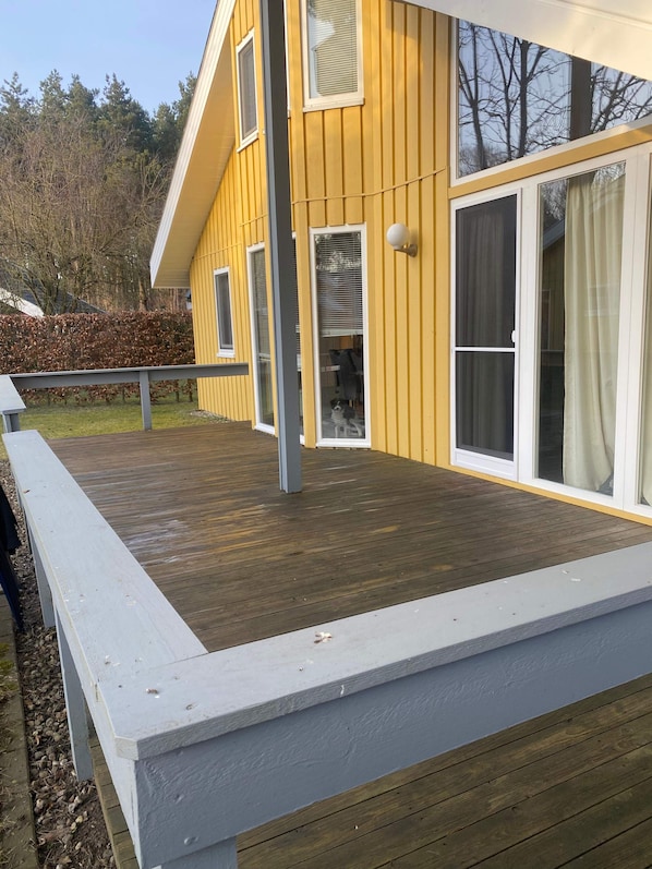 Una casa amarilla con terraza de madera y barandilla blanca.