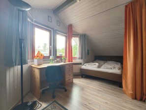 Ein Zimmer mit Holztisch, Stuhl, Bett und einem Fenster mit Vorhängen.