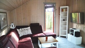 A wooden-paneled room with a red leather sofa, a white coffee table, a bookshelf, and a TV mounted on the wall. - Wildgans 113 - Klassisches Skandinavisches Ferienhaus für bis zu 6 Personen (Mirow)