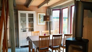 A dining area with a wooden table and chairs, a cabinet with dishes, a hanging lamp, and a wood stove. - Wildgans 113 - Klassisches Skandinavisches Ferienhaus für bis zu 6 Personen (Mirow)