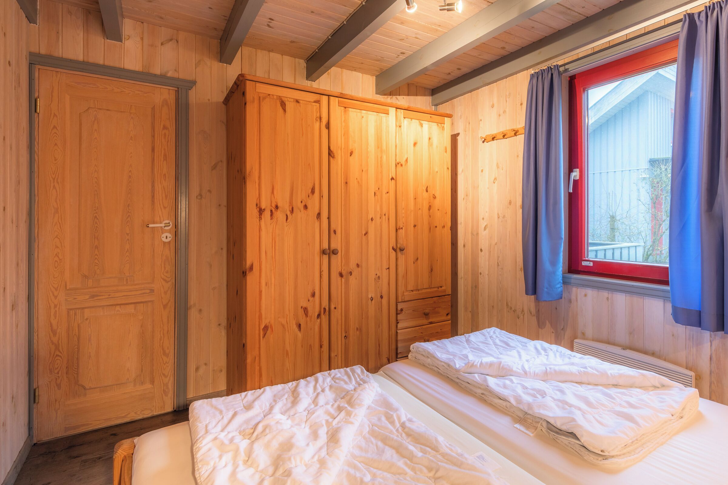 A wooden room with a bed, a wardrobe, and a window with curtains.