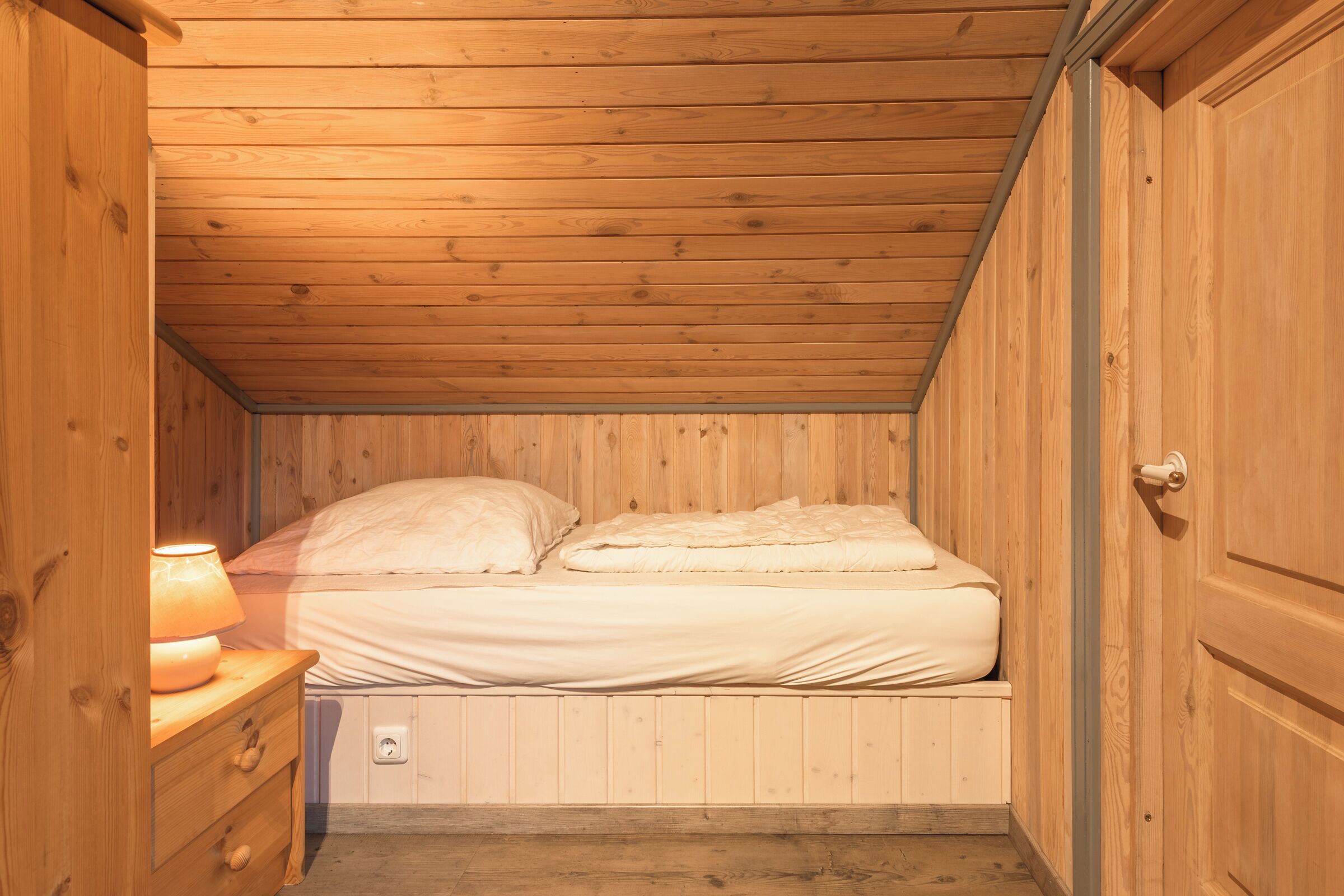 A wooden-paneled bedroom with a bed, a nightstand, and a wall socket.